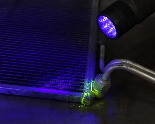 UV dye glowing at an AC condenser seam and fitting during leak inspection